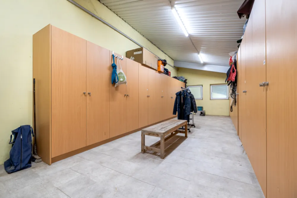 Reihe heller Spind-Kästen an der Stallwand mit Sitzbank davor