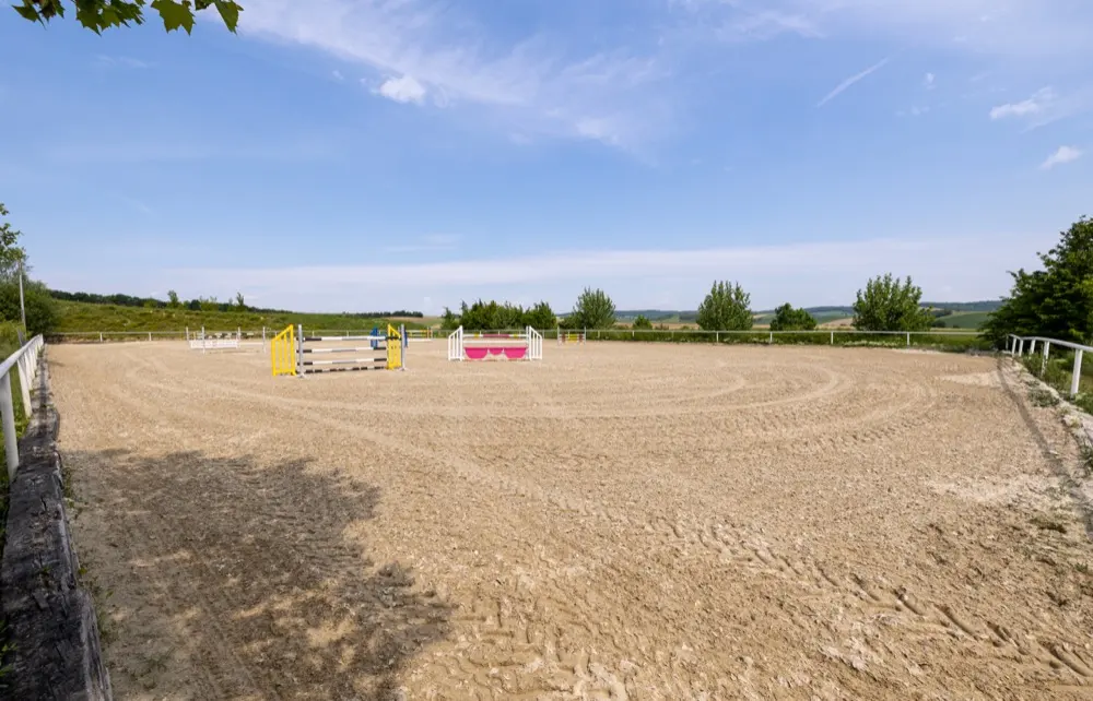 Weiter Springplatz mit Sandboden, Hindernisse am Rand, dahinter Felder