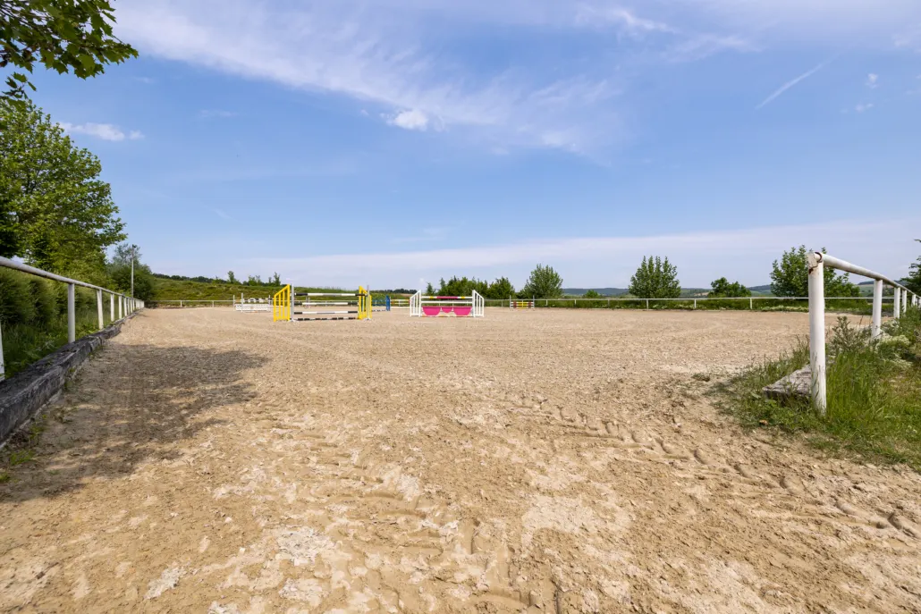 Weiter Springplatz mit Sandboden, aufgebauten Hindernissen und Feldern im Hintergrund